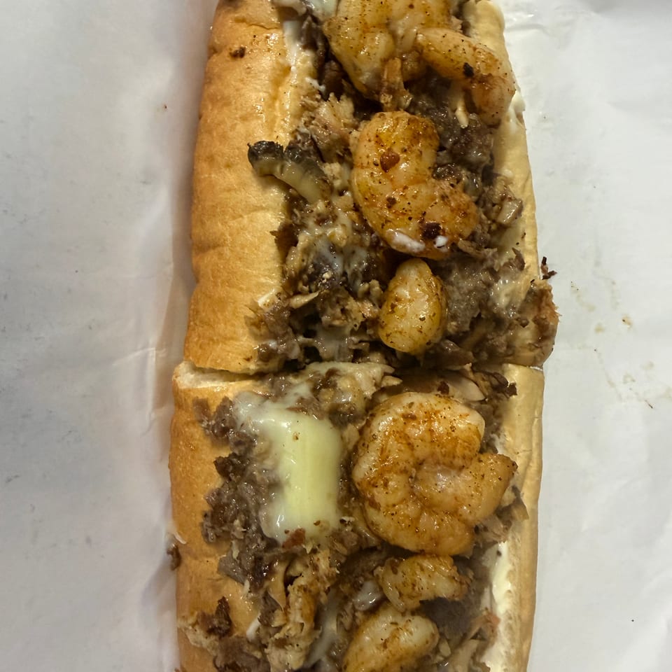 Close-up of a toasted sub sandwich filled with seasoned shrimp, chopped meat, and melted cheese.