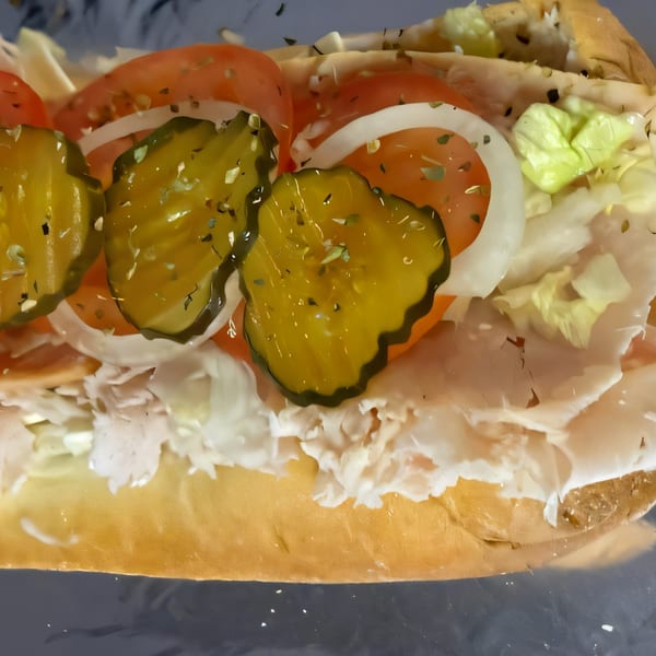 Close-up of a Philly Boyz cheesesteak with pickles, tomatoes, onions, and lettuce.