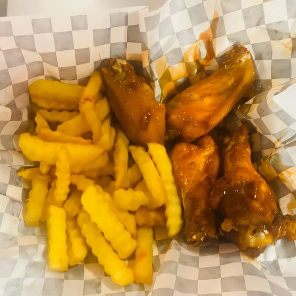 Crinkle-cut fries and saucy chicken wings served in a paper-lined basket from Philly Boyz Cheesesteaks.