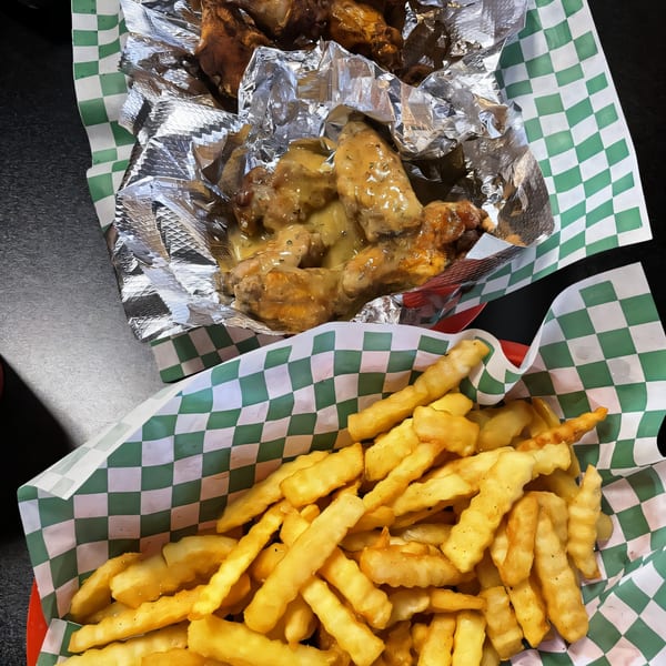 Two baskets of food, one with golden fries and the other with saucy chicken wings.