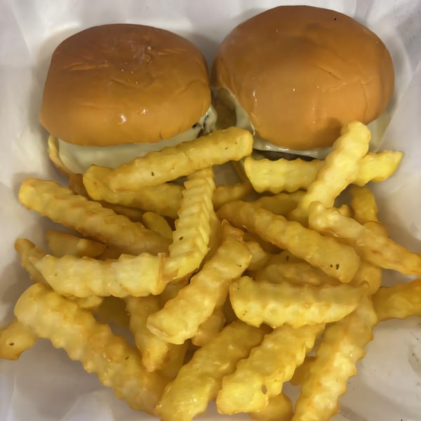 Two cheesesteak sliders with melted cheese and a side of golden crinkle-cut fries in a white basket.