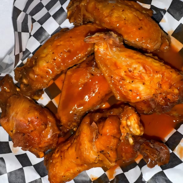 Close-up of several buffalo chicken wings drenched in orange sauce, served in a checkered paper-lined basket.