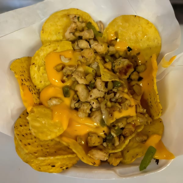 Cheesesteak nachos with melted cheese, chicken, and green peppers in a white container.