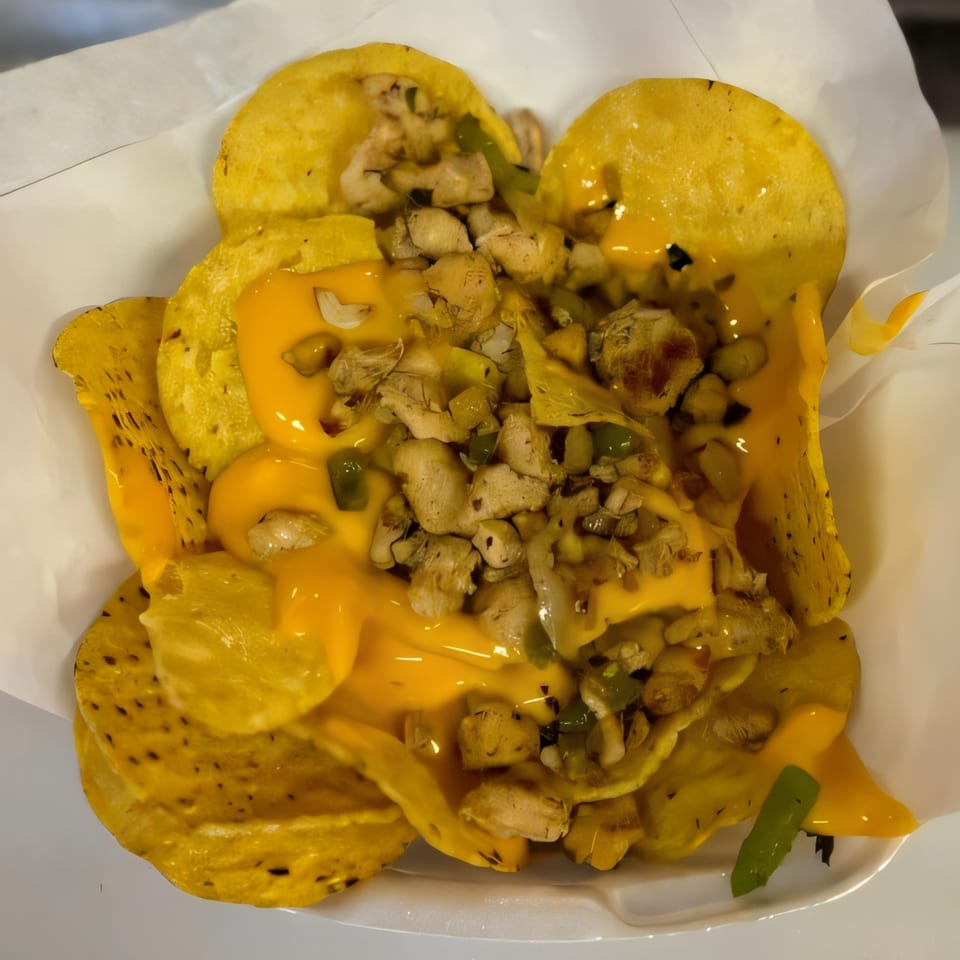 Cheesesteak nachos with melted cheese, chicken, and green peppers in a white container.
